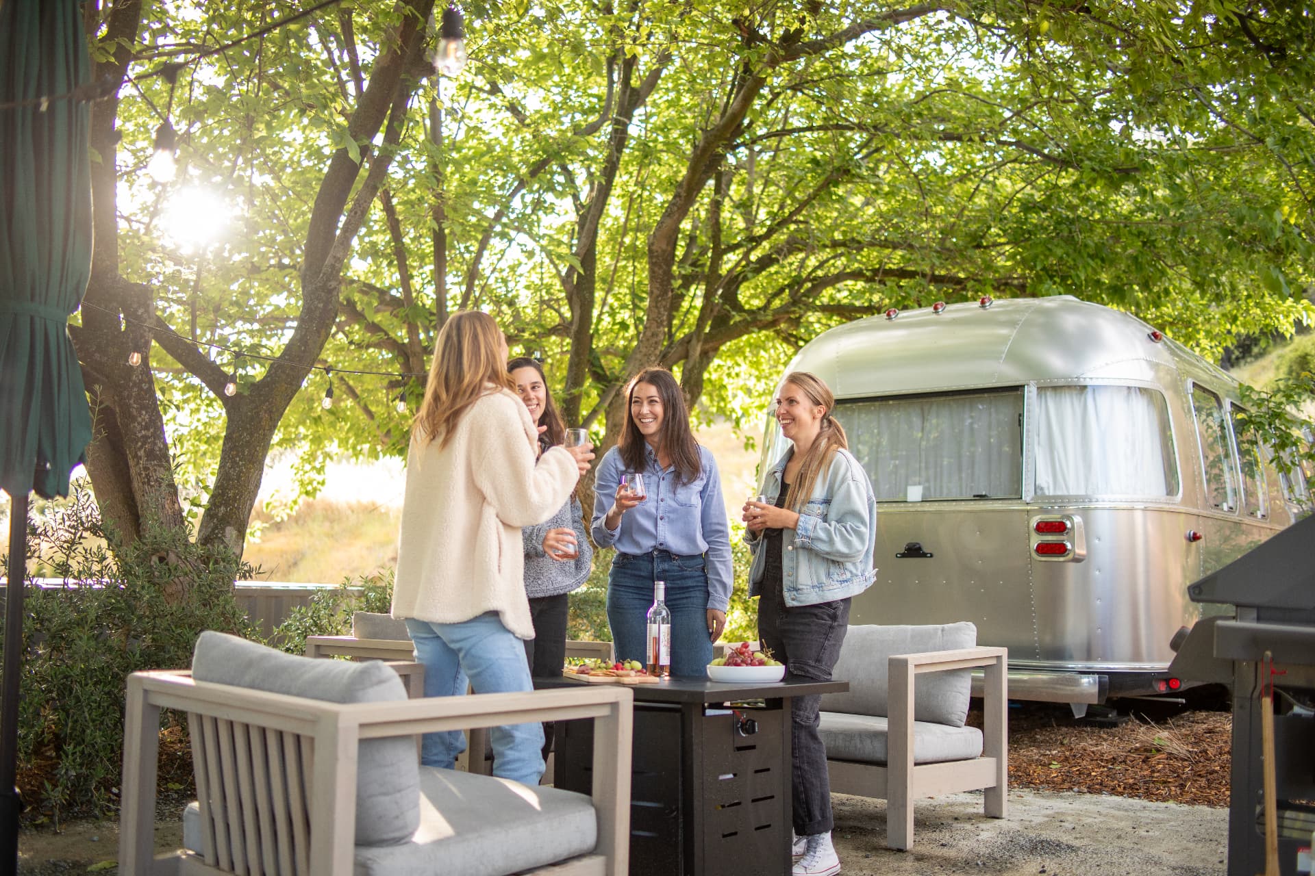 Sunlight through oak branches over an Airstream patio with lounge seating